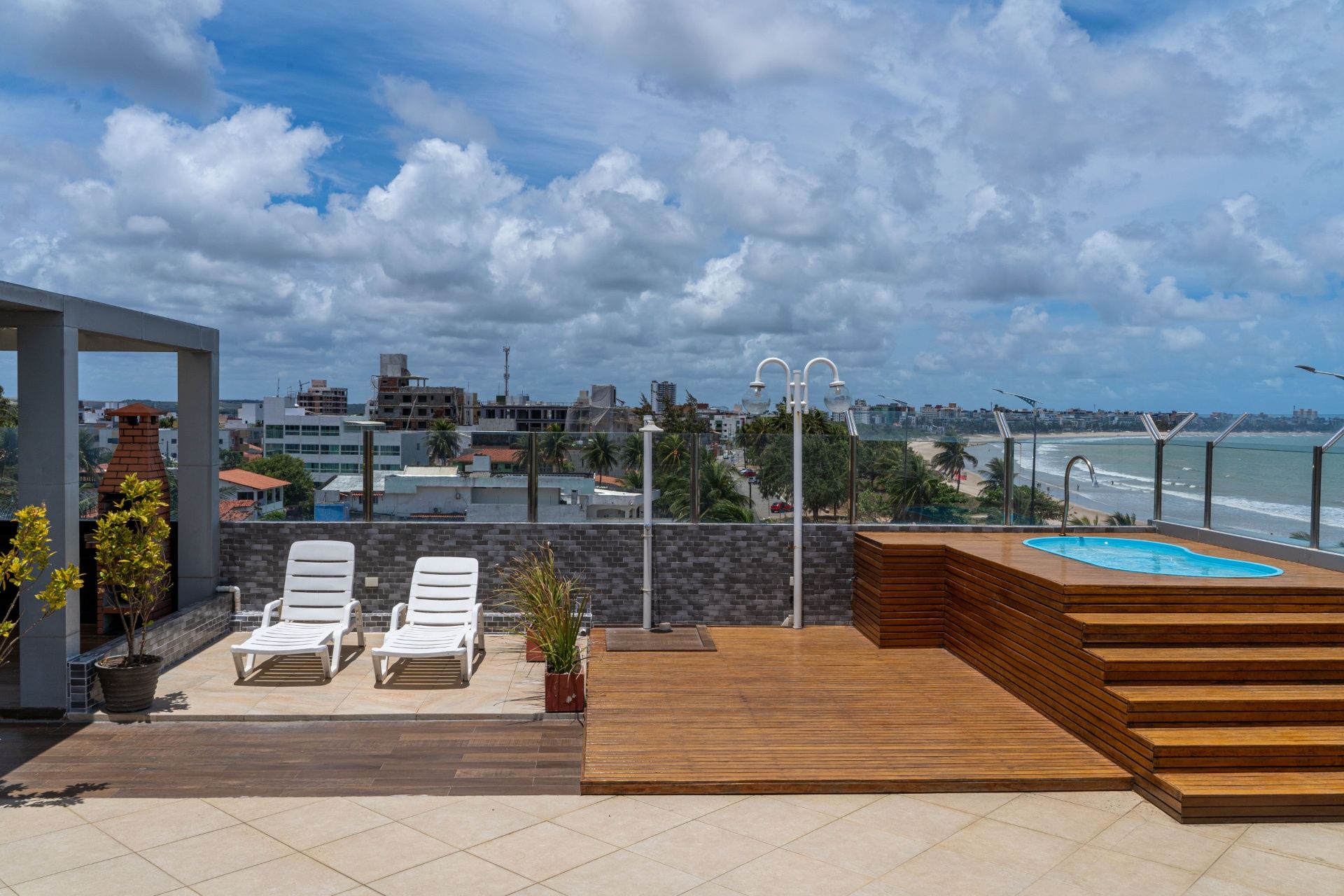 Terraço com piscina na cobertura, espreguiçadeiras, degraus de madeira e vista para o horizonte da cidade sob um céu nublado.