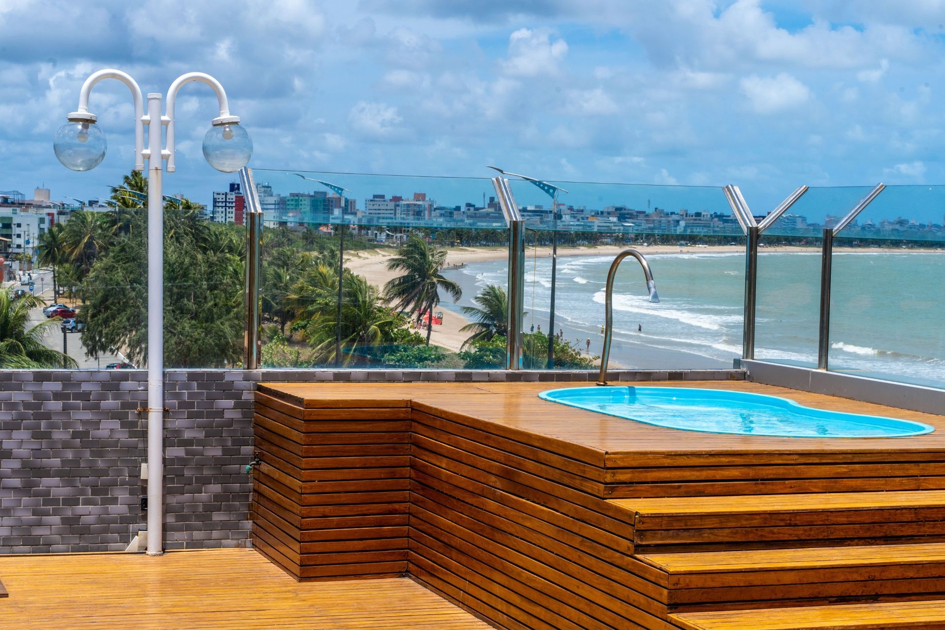 Terraço da piscina à beira-mar com vista para o oceano e palmeiras sob um céu azul nublado.