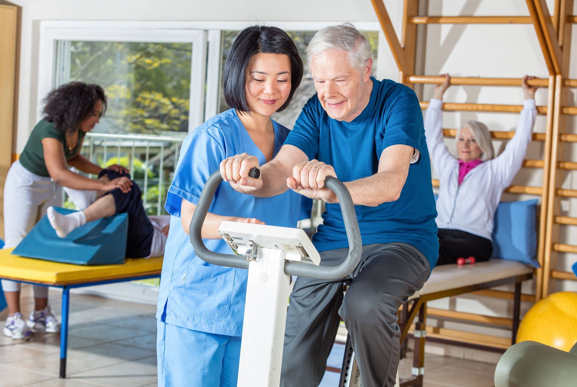 Physical therapist helping a patient on an exercise bike in a bright rehab room