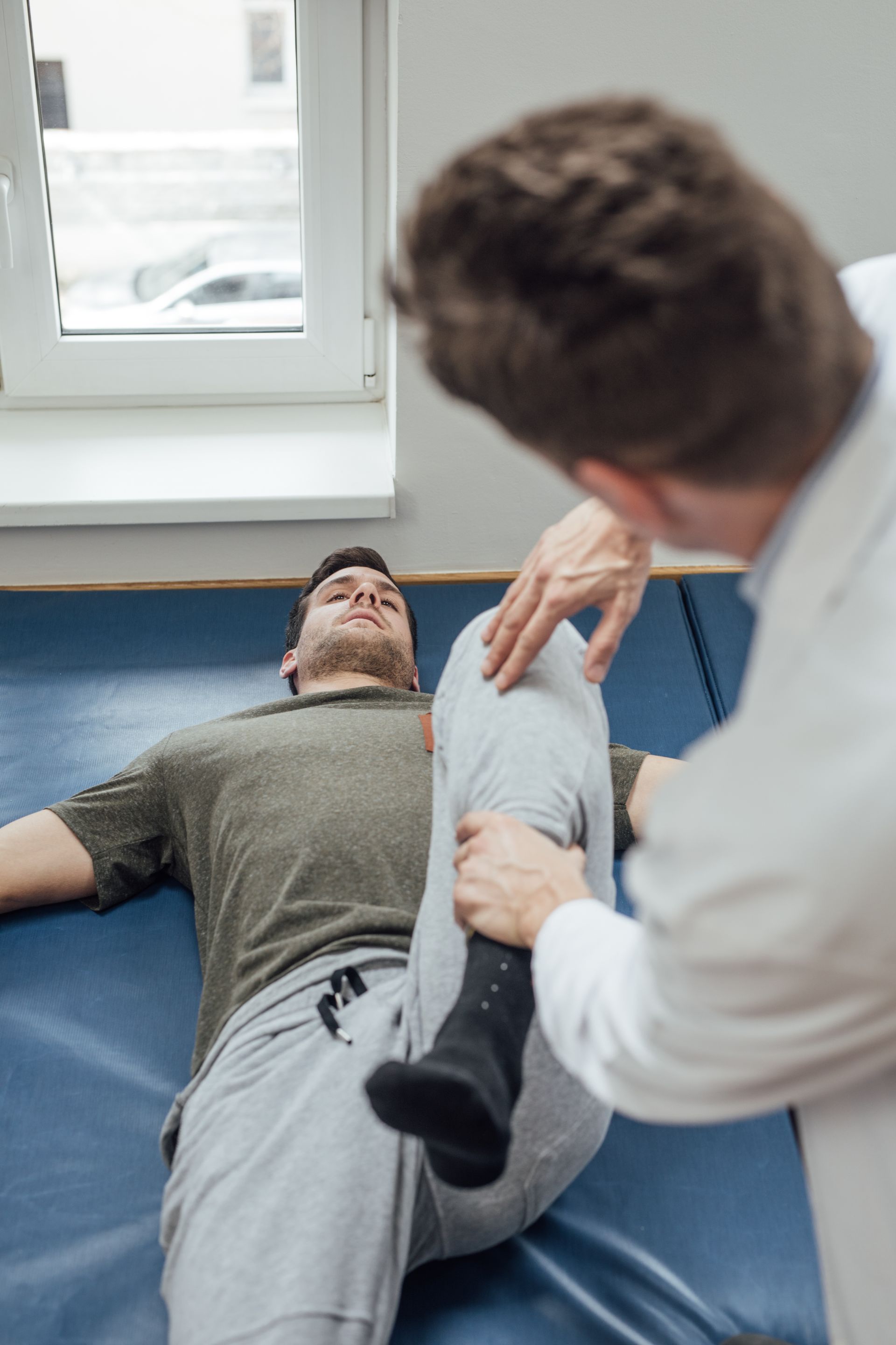 Physical therapist stretching a patient’s leg on a blue mat in a clinic.