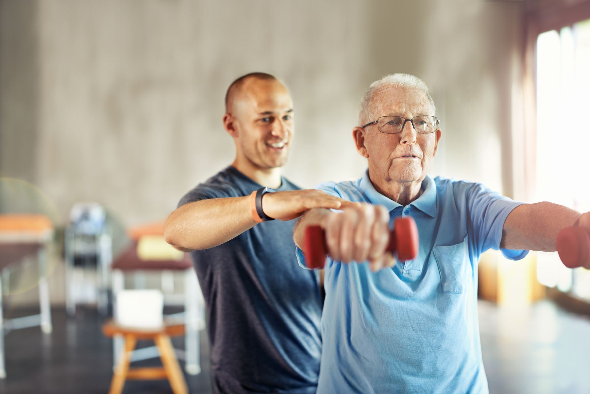 Two people exercising with dumbbells in a bright gym, one guiding the other