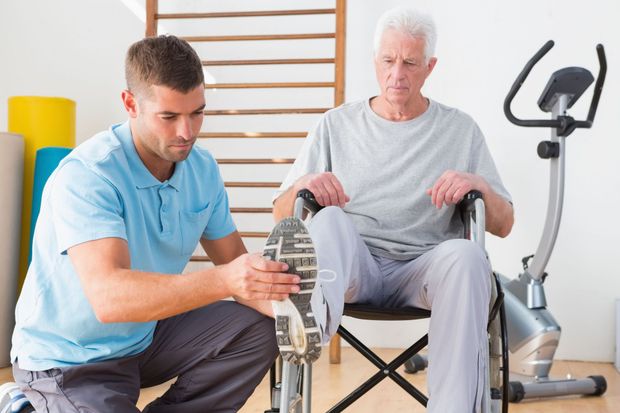 Physical therapist helping a seated patient stretch his foot in a rehab room with exercise equipment Physical therapist helping a seated patient stretch his foot in a rehab room with exercise equipment
