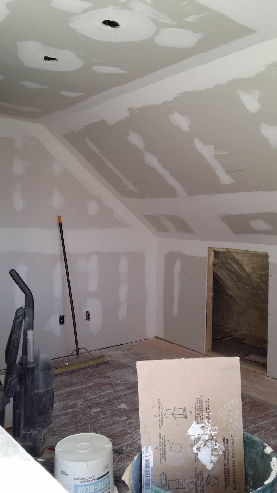 A room with a vacuum cleaner and a bucket of paint on the floor.
