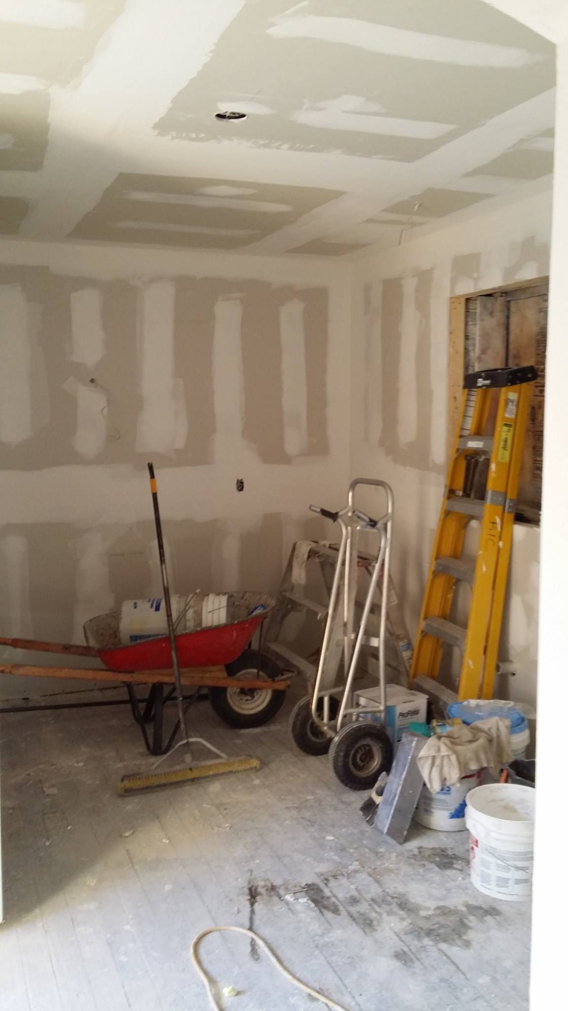 A room with a ladder and a wheelbarrow in it.