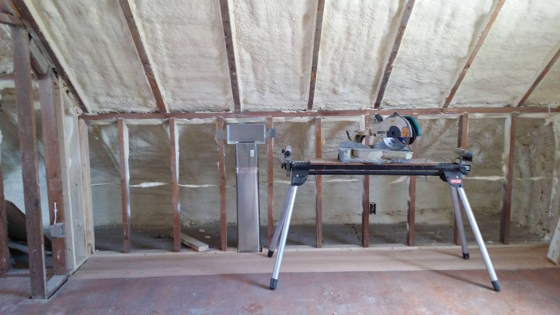 A sliding miter saw is sitting on a workbench in an attic.