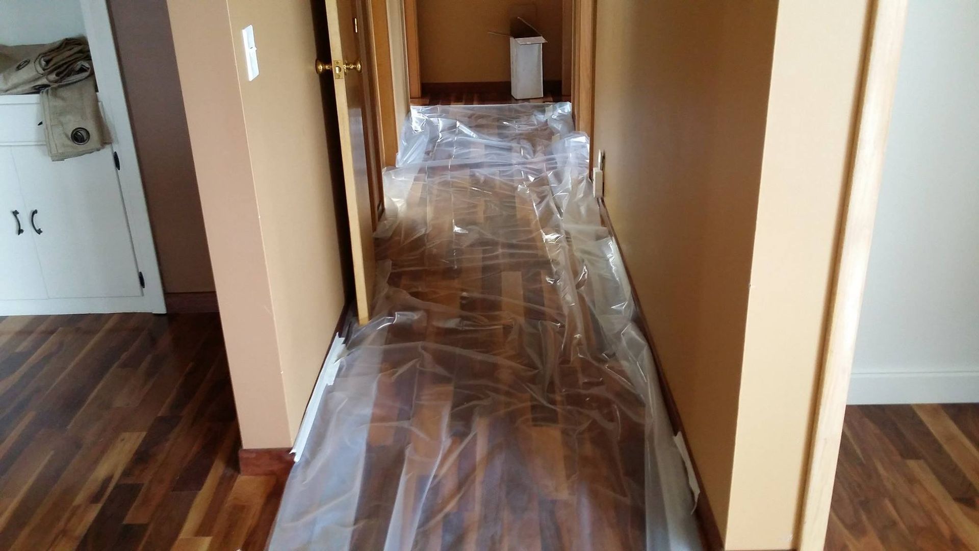 A hallway with hardwood floors and plastic covering the floor.
