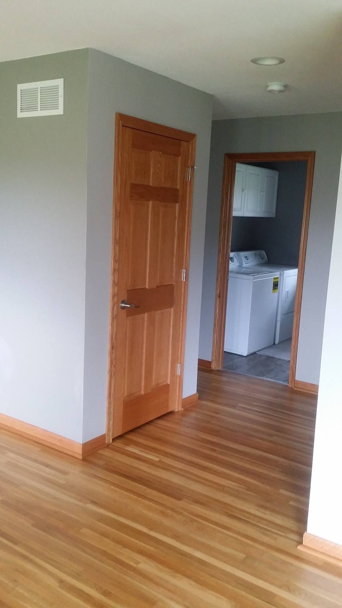 A hallway with hardwood floors and a laundry room with a washer and dryer.