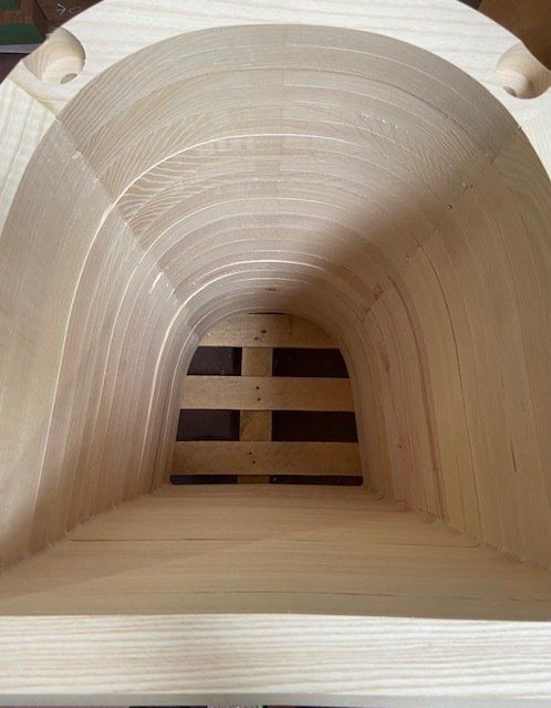 Vista interna di un tunnel o tubo in legno chiaro con apertura a persiana all'estremità opposta.