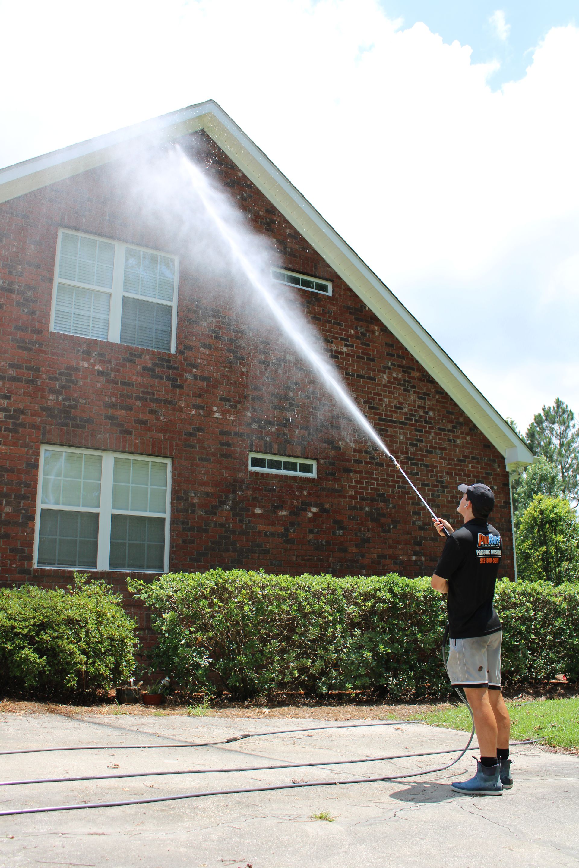 A person pressure washing a brick house on a sunny day.