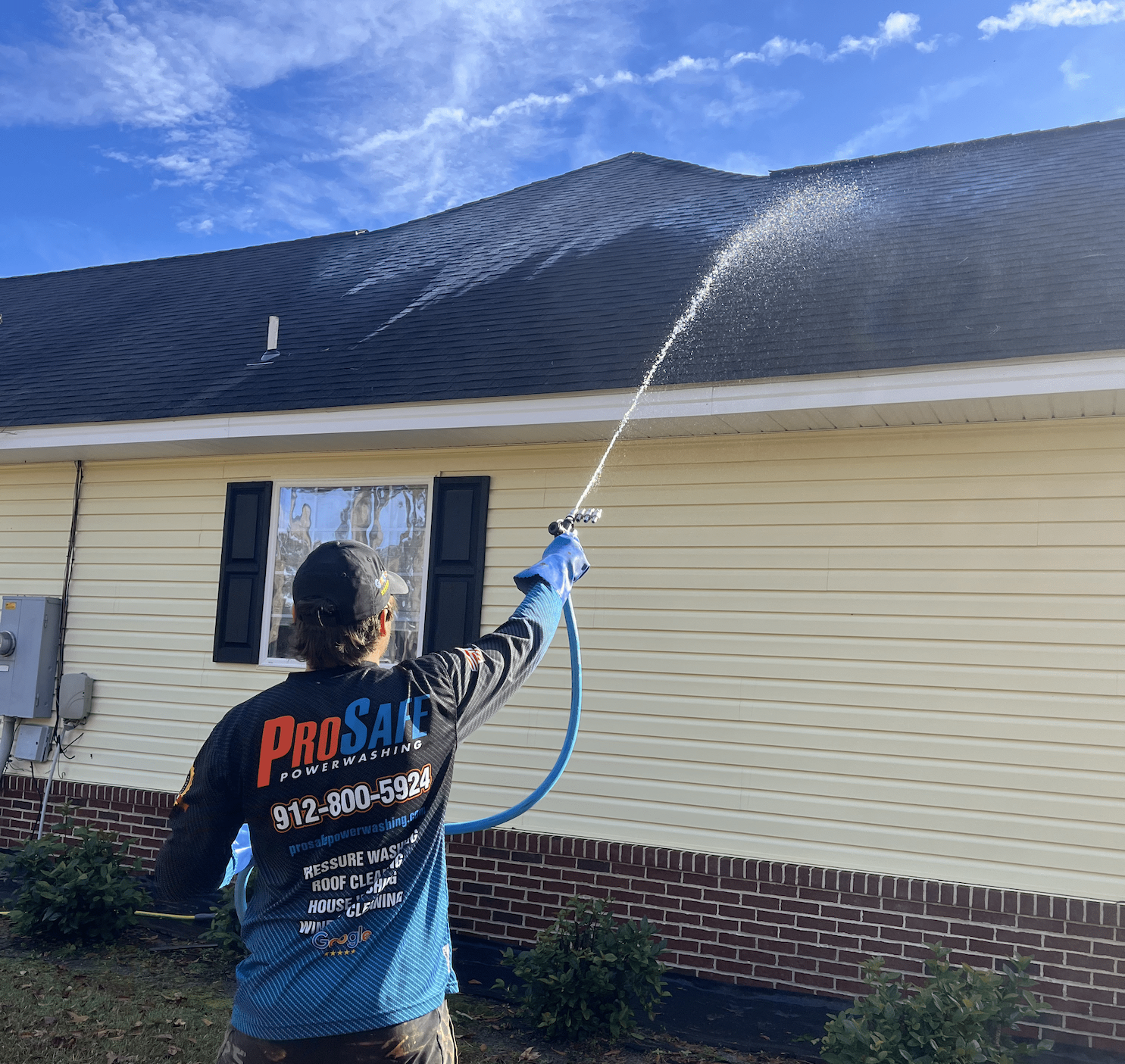 A man is spraying water on the roof of a house.