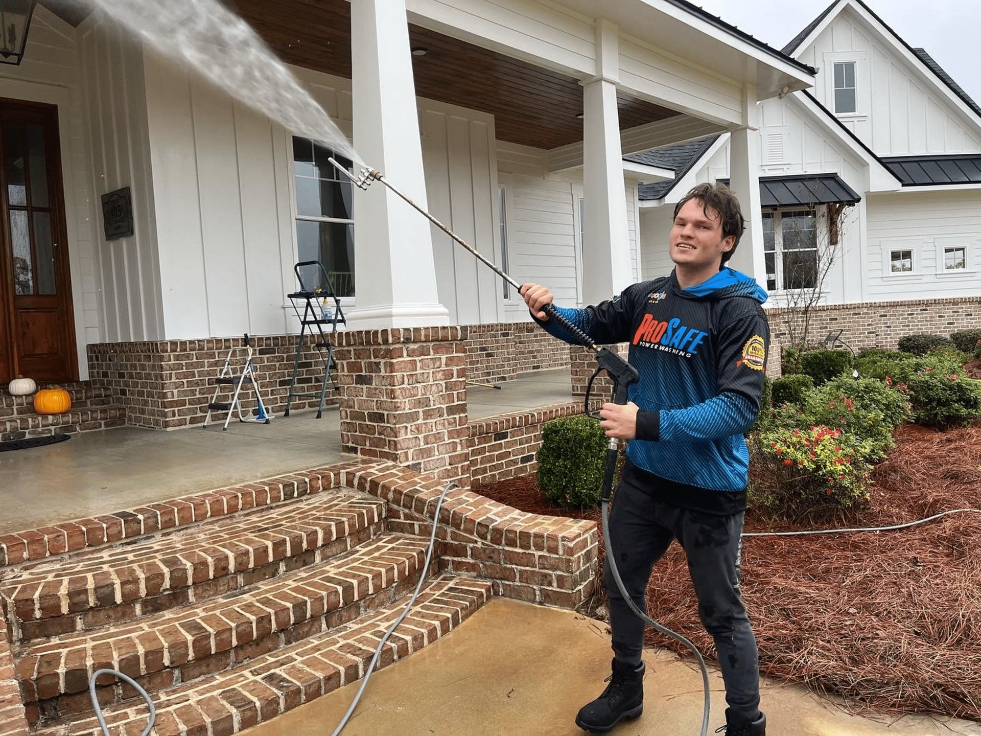 A man is using a pressure washer to clean the sidewalk in front of a house.