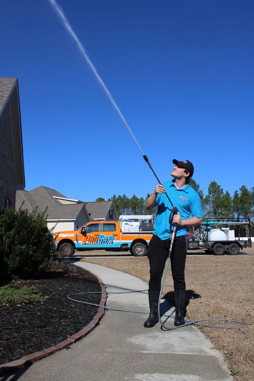 A person pressure washing a brick house on a sunny day.