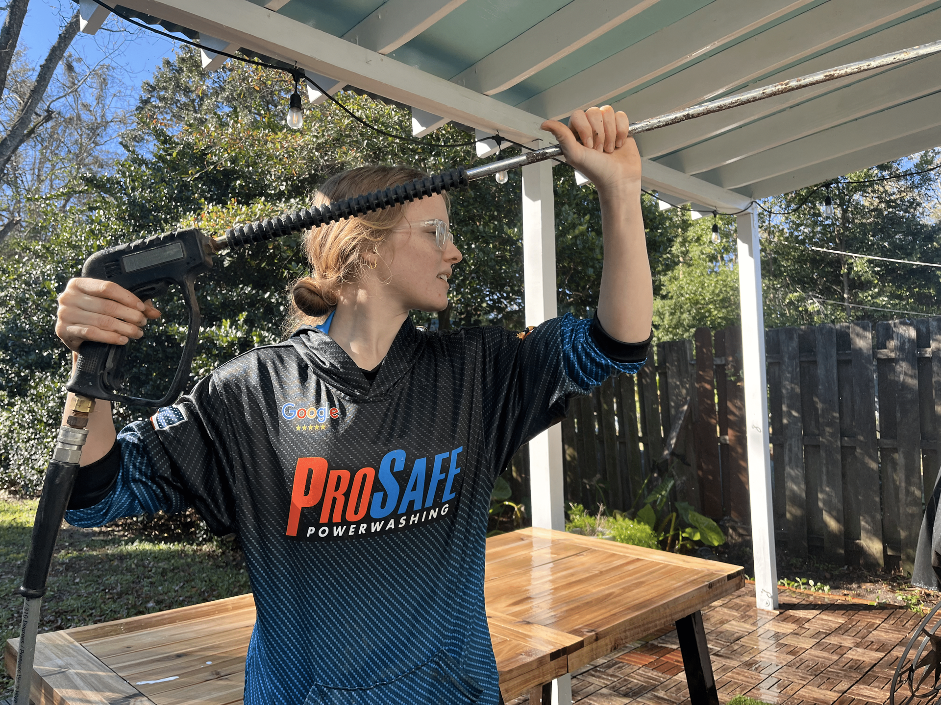 A woman is using a high pressure washer to clean a patio table.