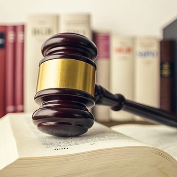Gavel on a Book — Norman, OK — Law Offices Of Mark S Cooper PC Gavel on open law book with a library background. Dark wood, gold band, neutral tones.