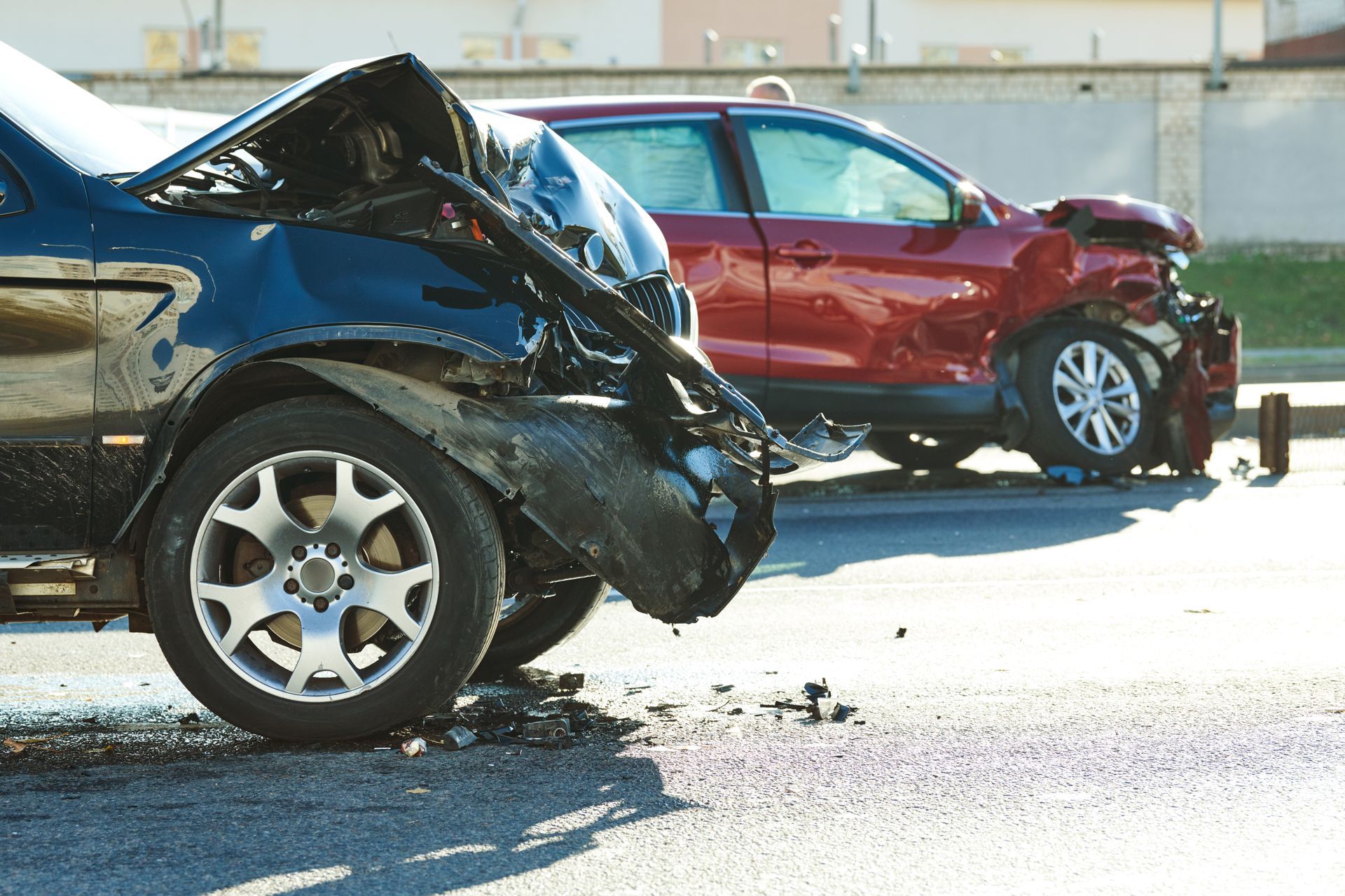 Two damaged cars stopped on a road after a collision, with crumpled fronts and debris nearby. Two damaged cars stopped on a road after a collision, with crumpled fronts and debris nearby.