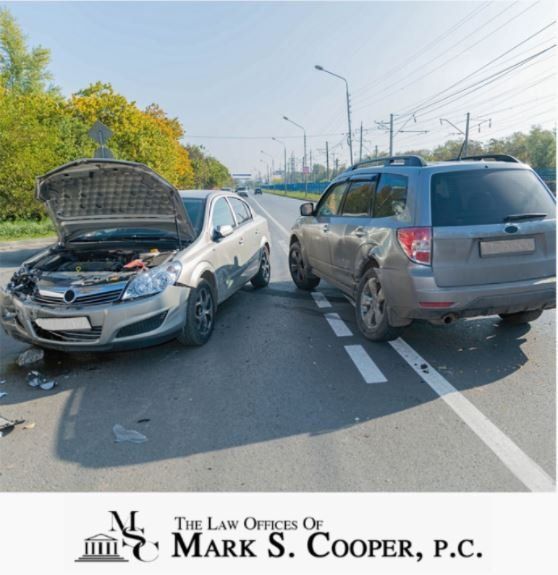 Two cars damaged in an accident on a road. One car's hood is up.