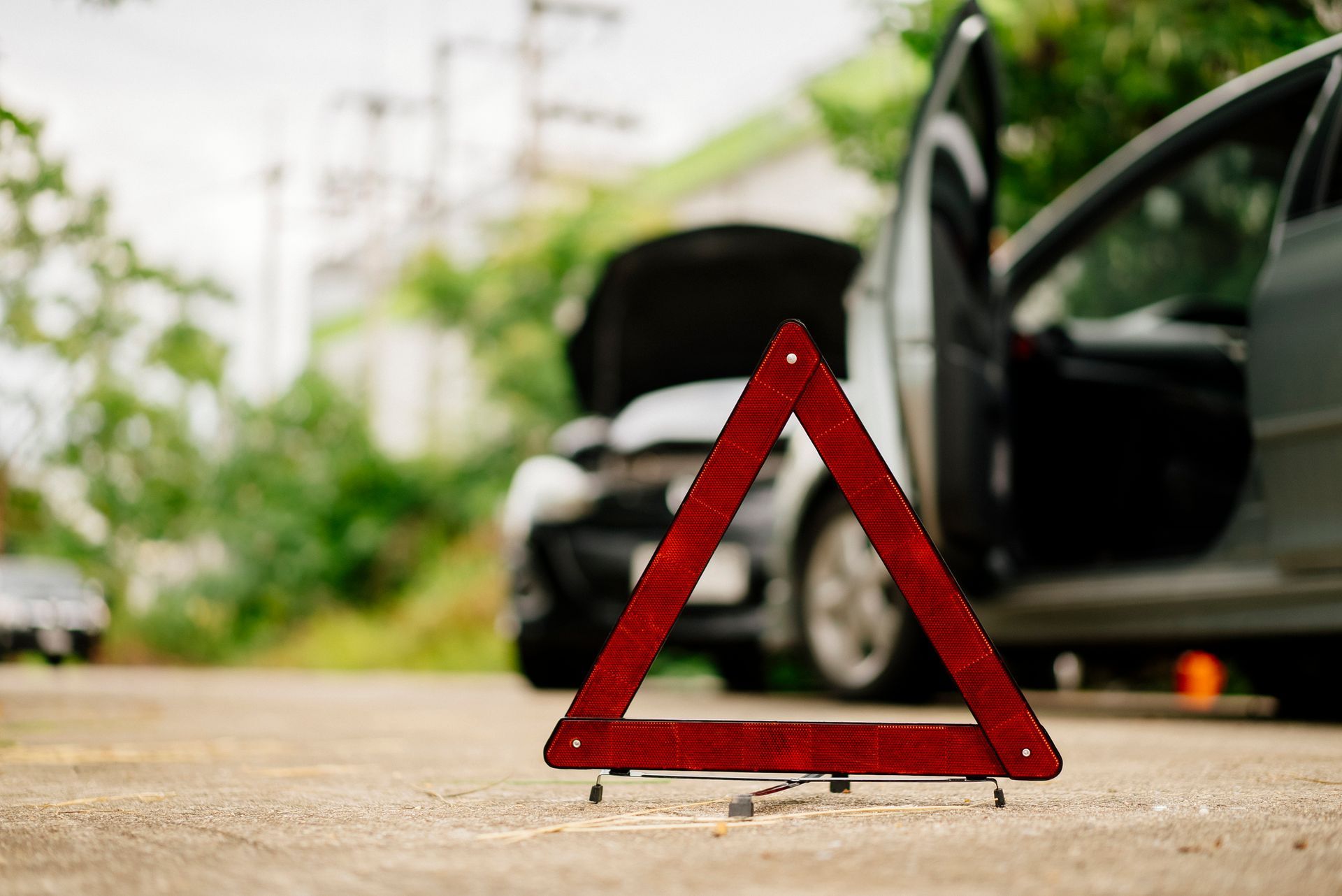 Red warning triangle in front of a disabled car with an open hood on a road.