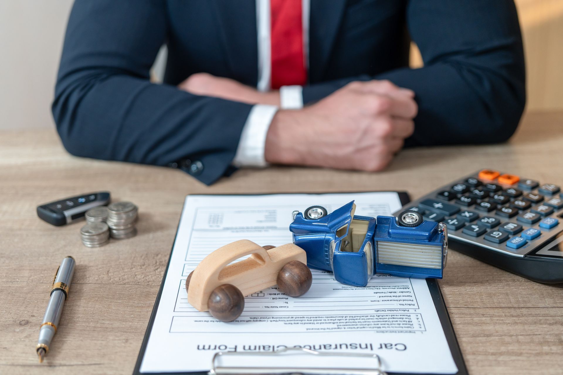 Man in suit with crossed arms, car insurance form, toy cars, and calculator on a desk.
