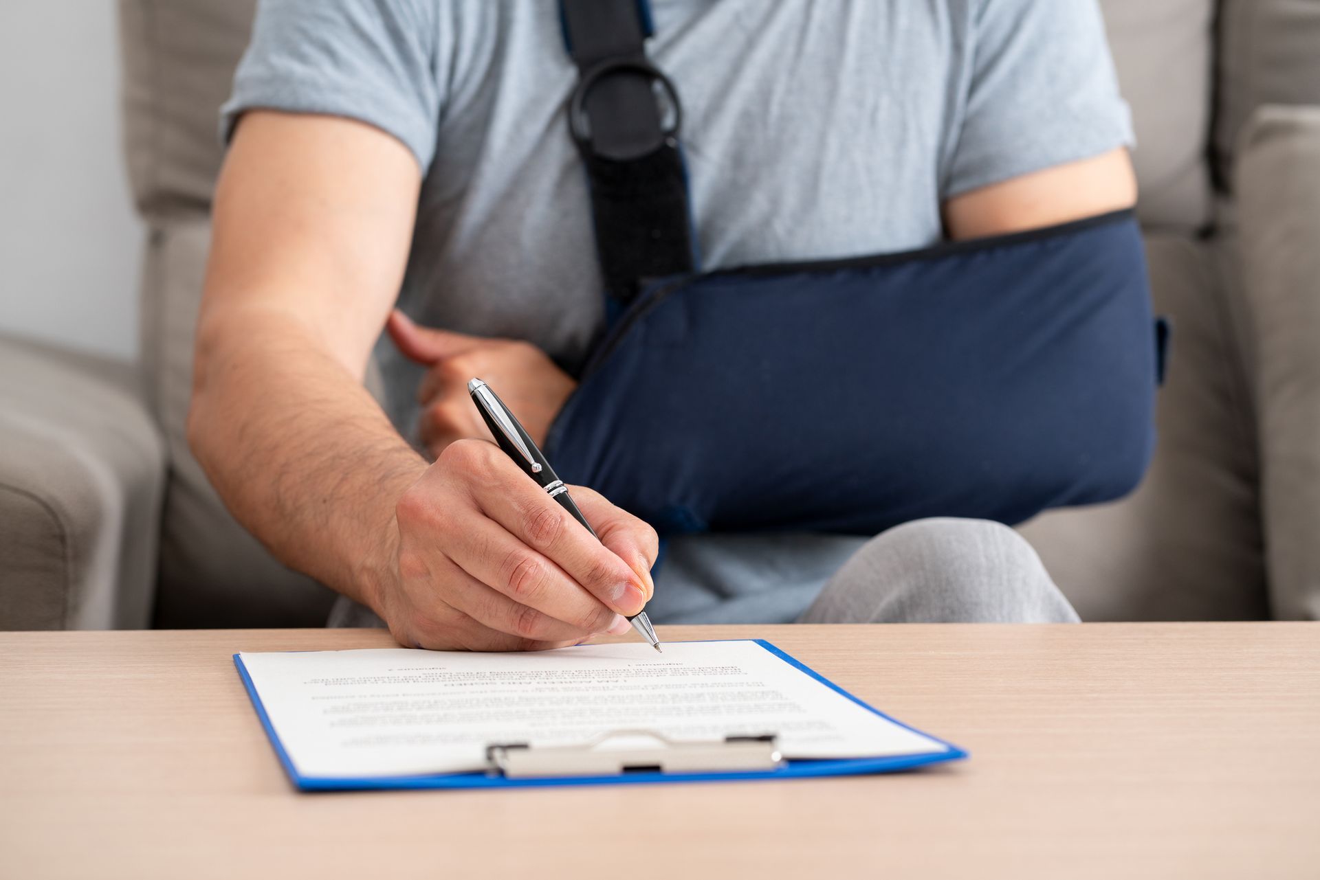 Man with arm in sling writing on a clipboard at a table.