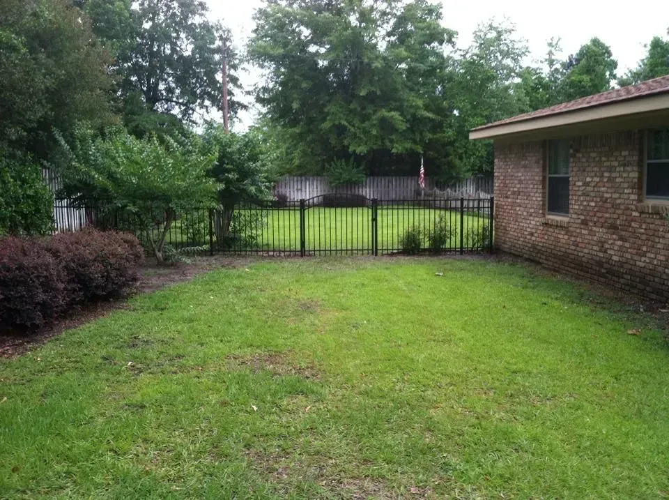 A backyard with a fence and a brick house in the background