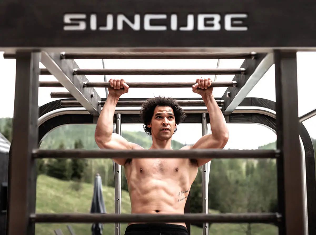 Un homme faisant des tractions sur une structure de fitness extérieure SUNCUBE dans un cadre montagneux.