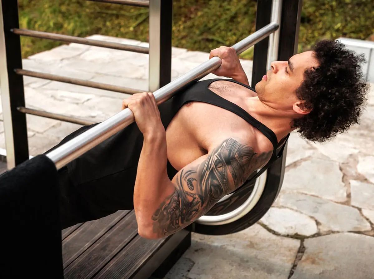 Un homme fait une traction sur une barre extérieure, montrant un tatouage sur le bras et un effort.