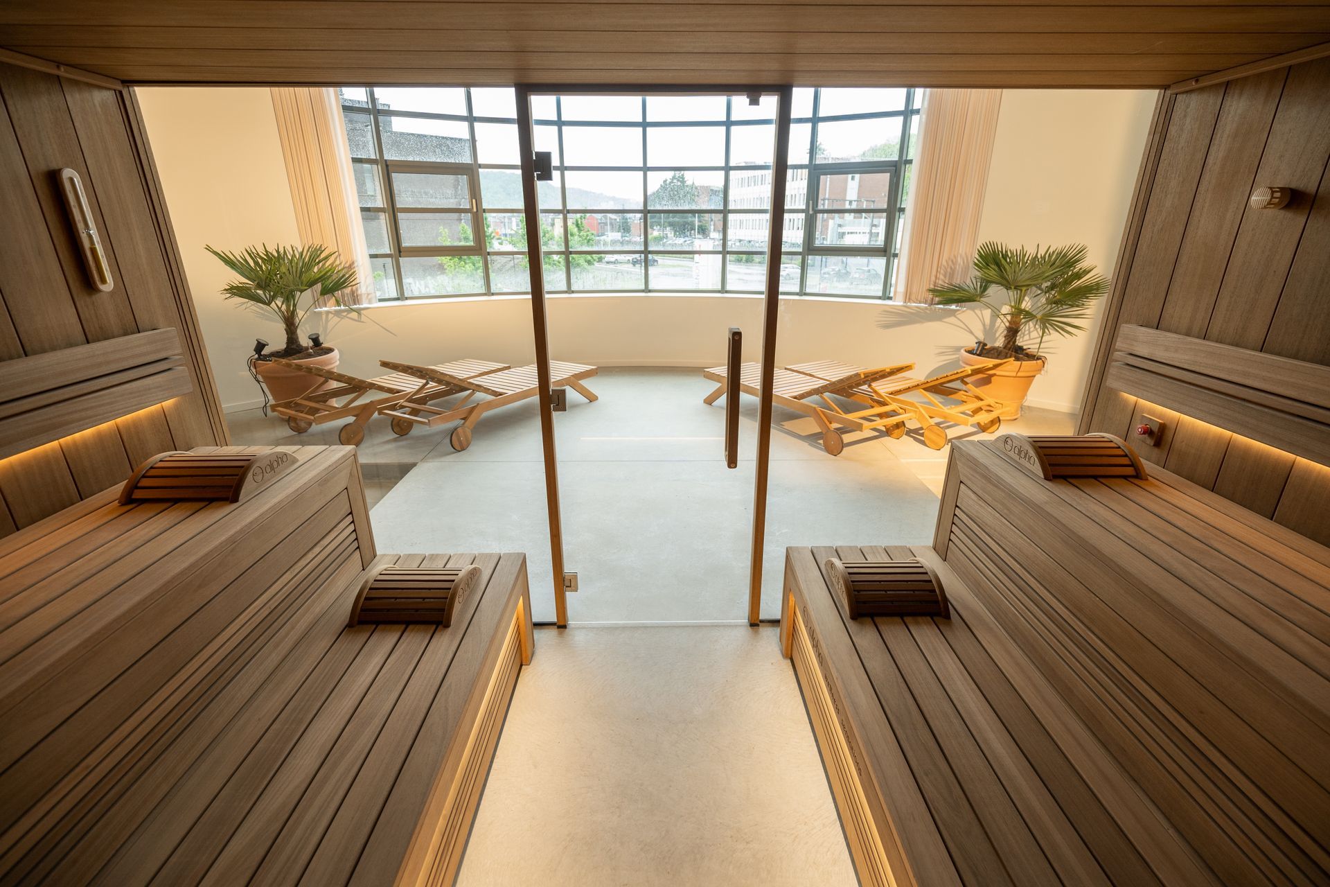Intérieur du sauna avec bancs en bois et chaises longues, donnant sur une vue à travers de grandes fenêtres.