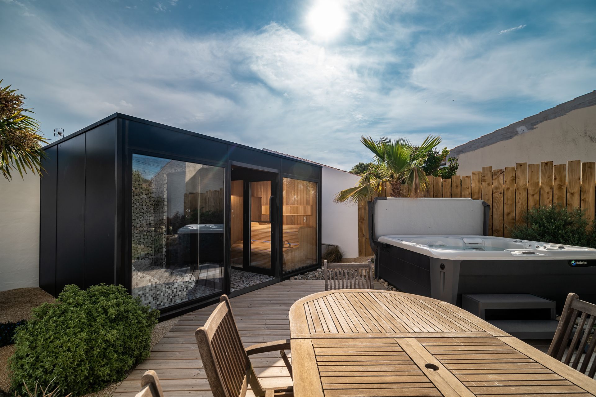 Spa extérieur avec cabine noire, bain à remous, terrasse en bois et ciel ensoleillé.