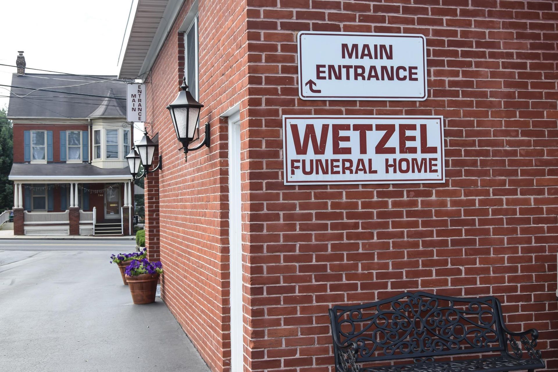 Brick exterior of Wetzel Funeral Home with a “Main Entrance” sign and potted flowers by the sidewalk