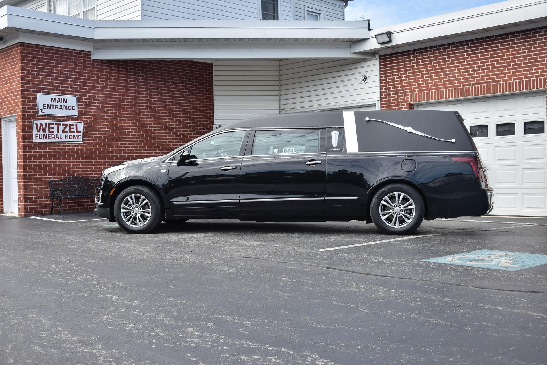 Black hearse parked beside a brick building with a garage door and handicap parking sign