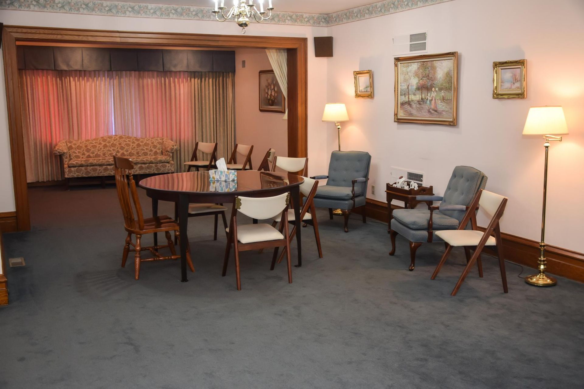 Empty living room with a dining table, chairs, lamps, and framed wall art under soft lighting