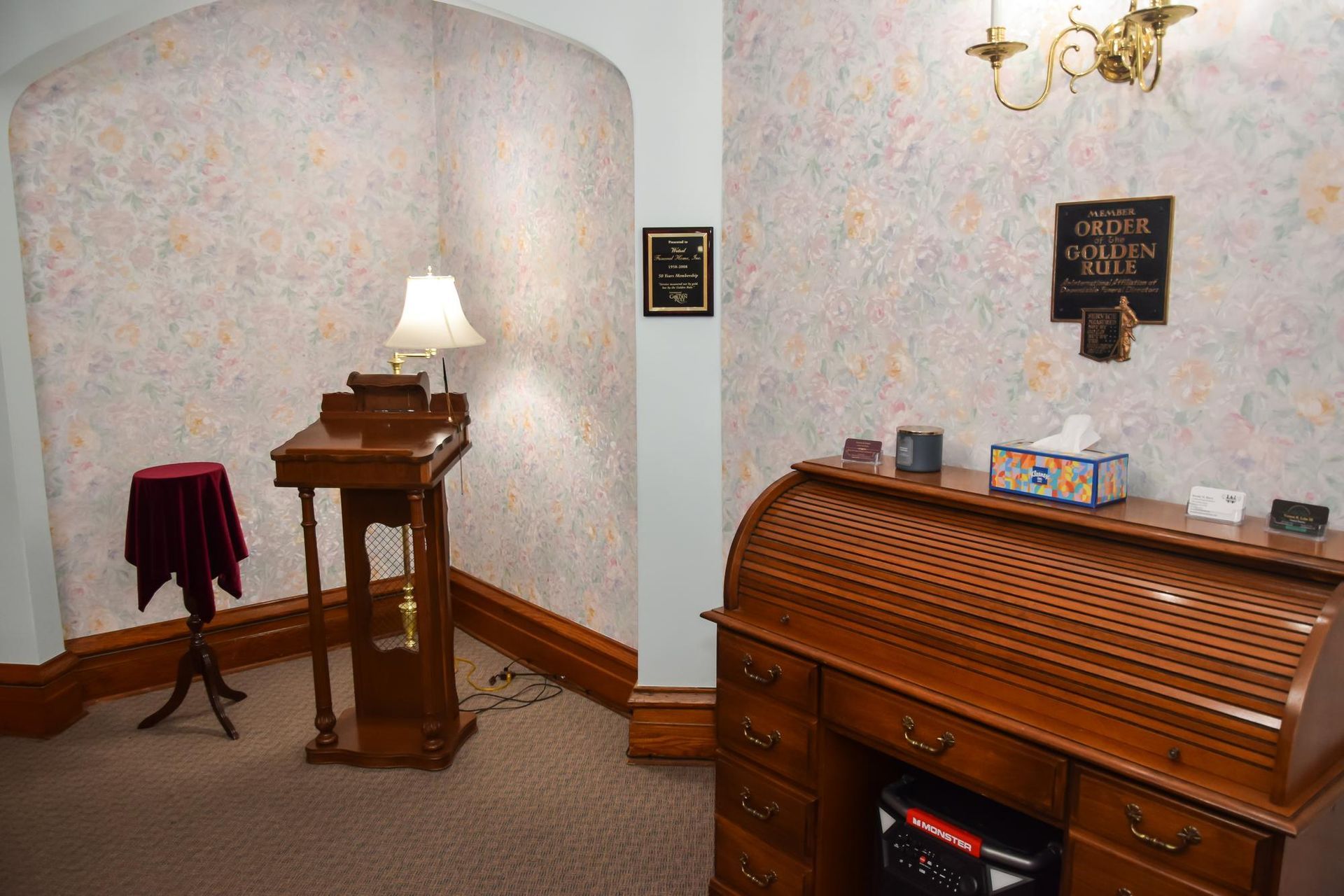 Historic room with wooden lectern, lamp, decorative wall plaques, and a polished organ console against patterned wallpaper