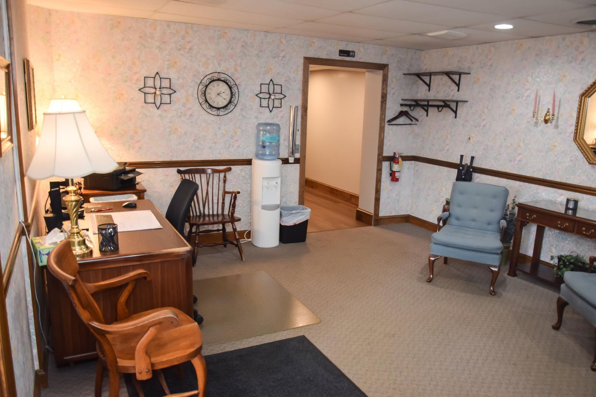 Cozy living room with desk, rocking chair, blue armchair, wall decor, and doorway to a hall