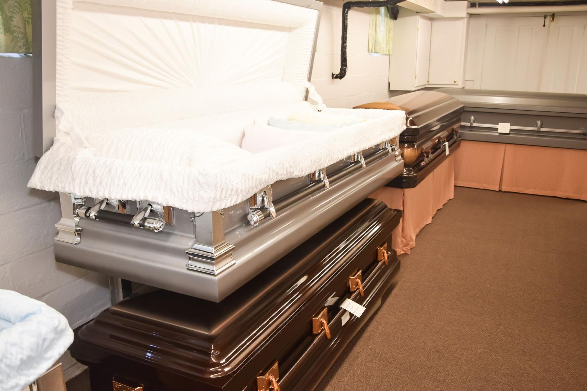 Open casket funeral room with silver and dark wood coffins lined along the wall