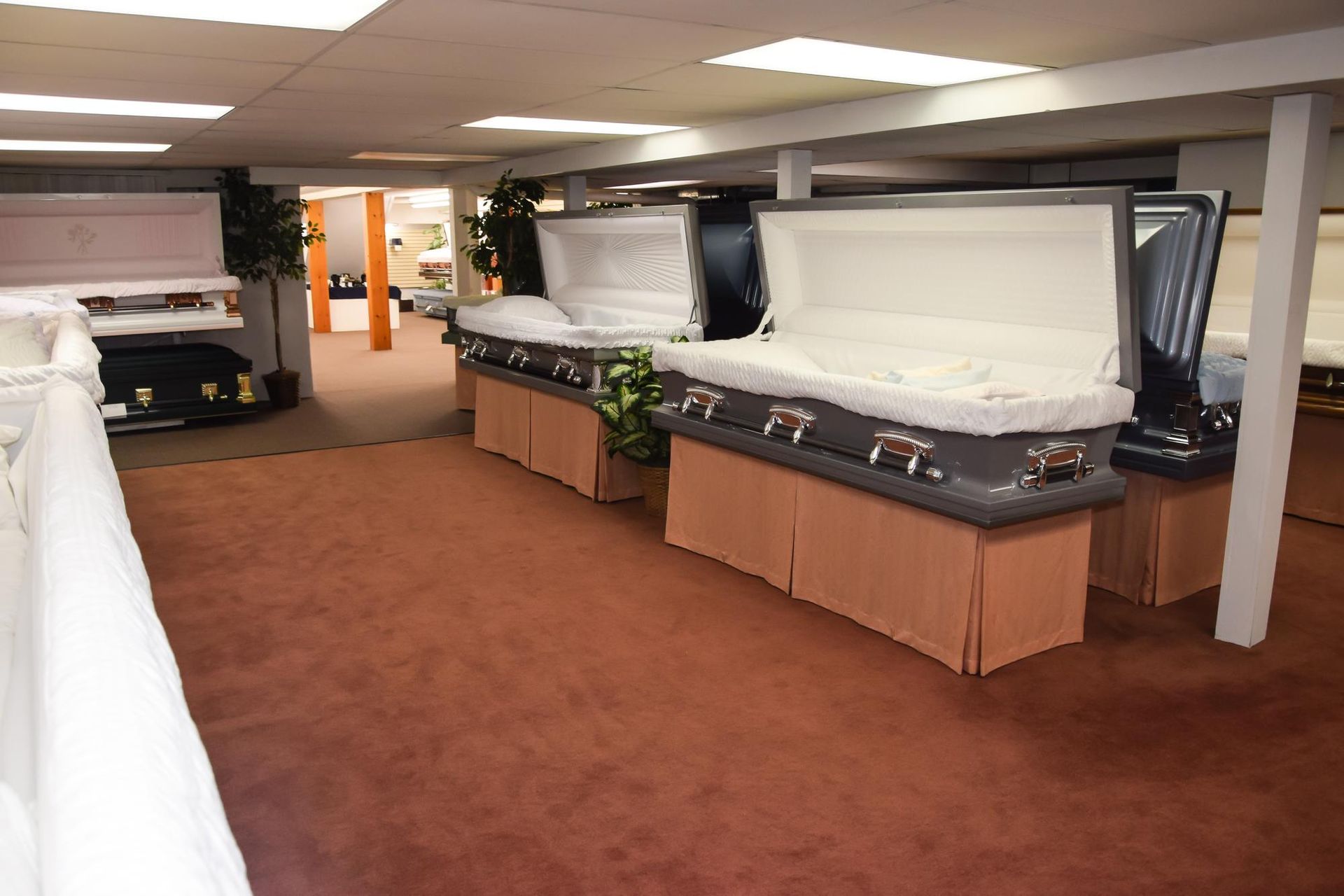 Coffin showroom with open caskets on display in a carpeted room