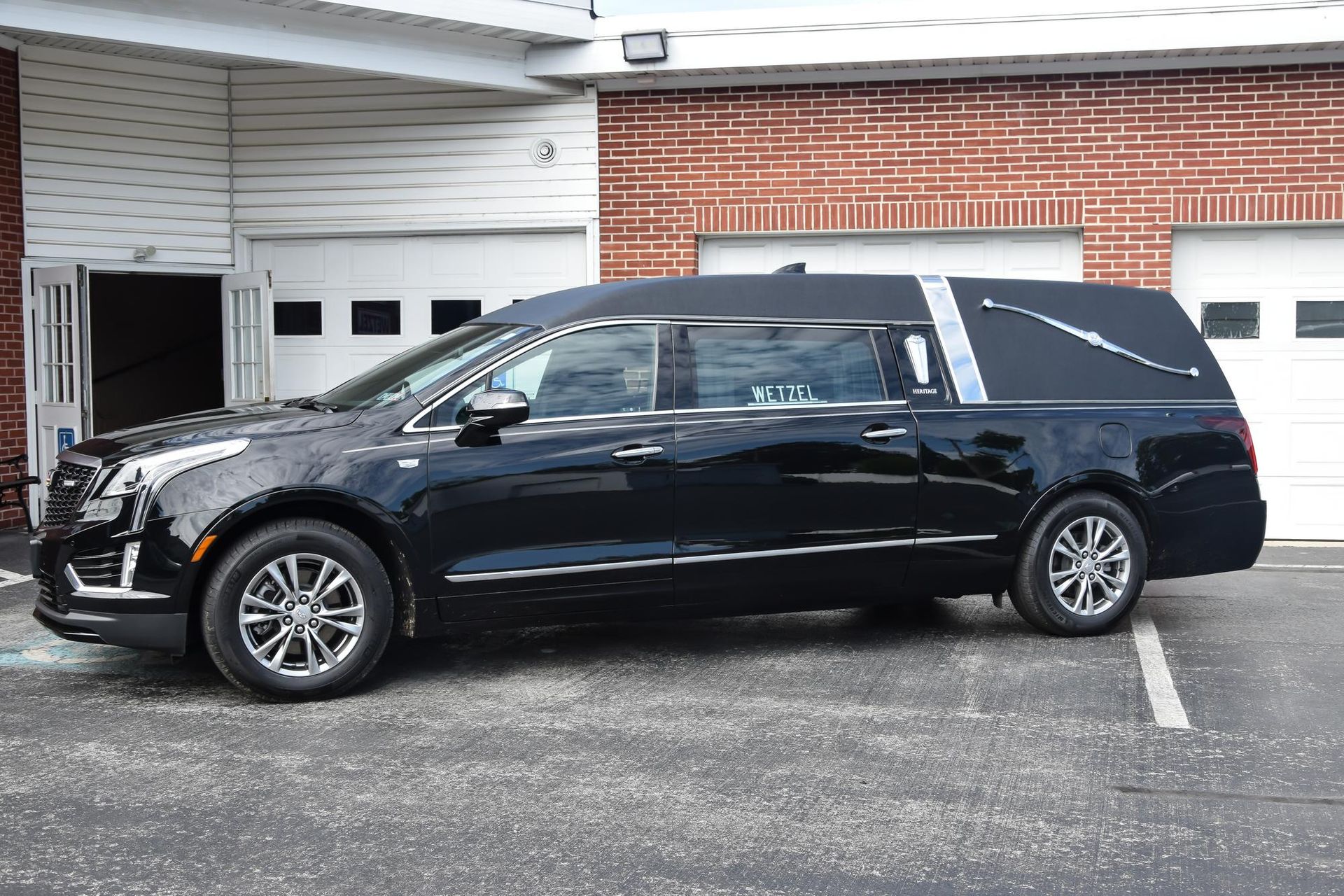 Black hearse parked outside a brick building with open garage doors