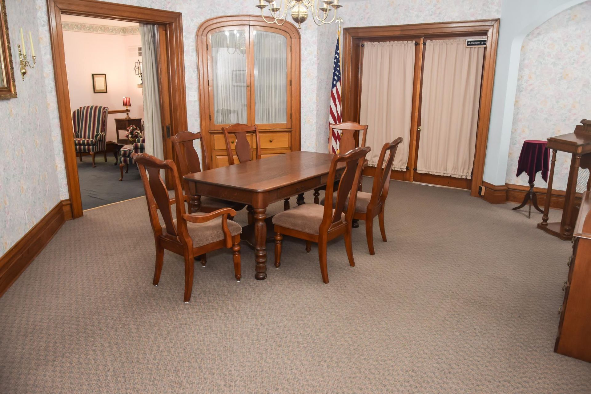 Dining room with wooden table and chairs, beige carpet, and glass-front cabinet by a doorway.