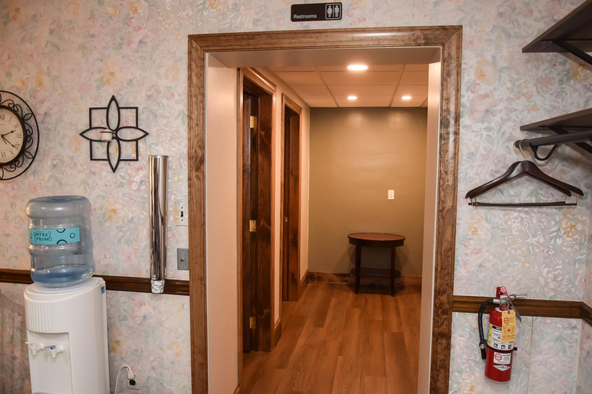 Hallway with wood floors, open door to a room, water cooler, coat hooks, and fire extinguisher.