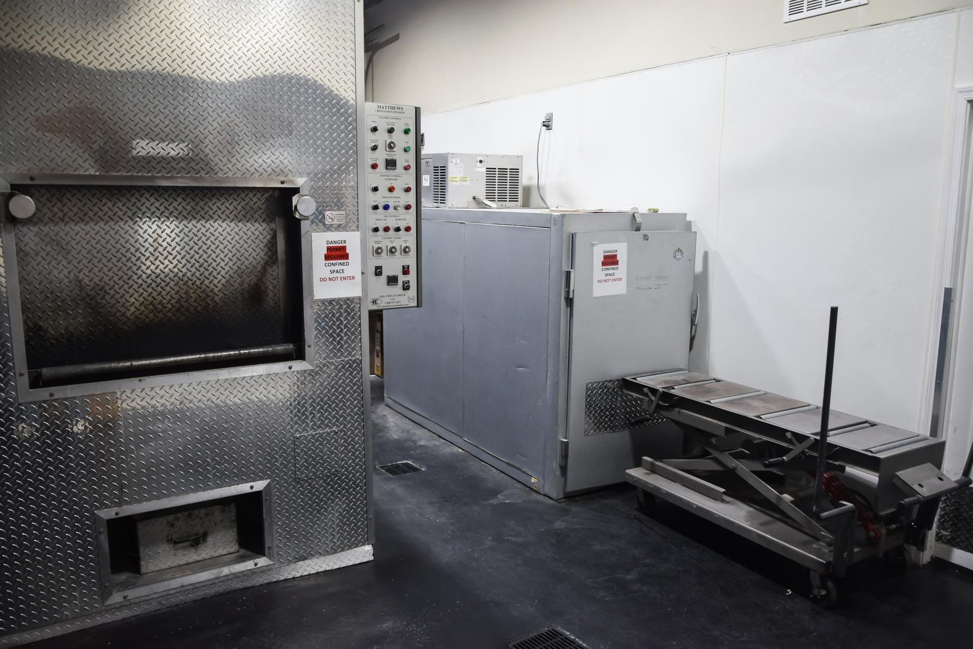 Industrial room with metal equipment, a large gray machine, and a wheeled cart on a concrete floor.