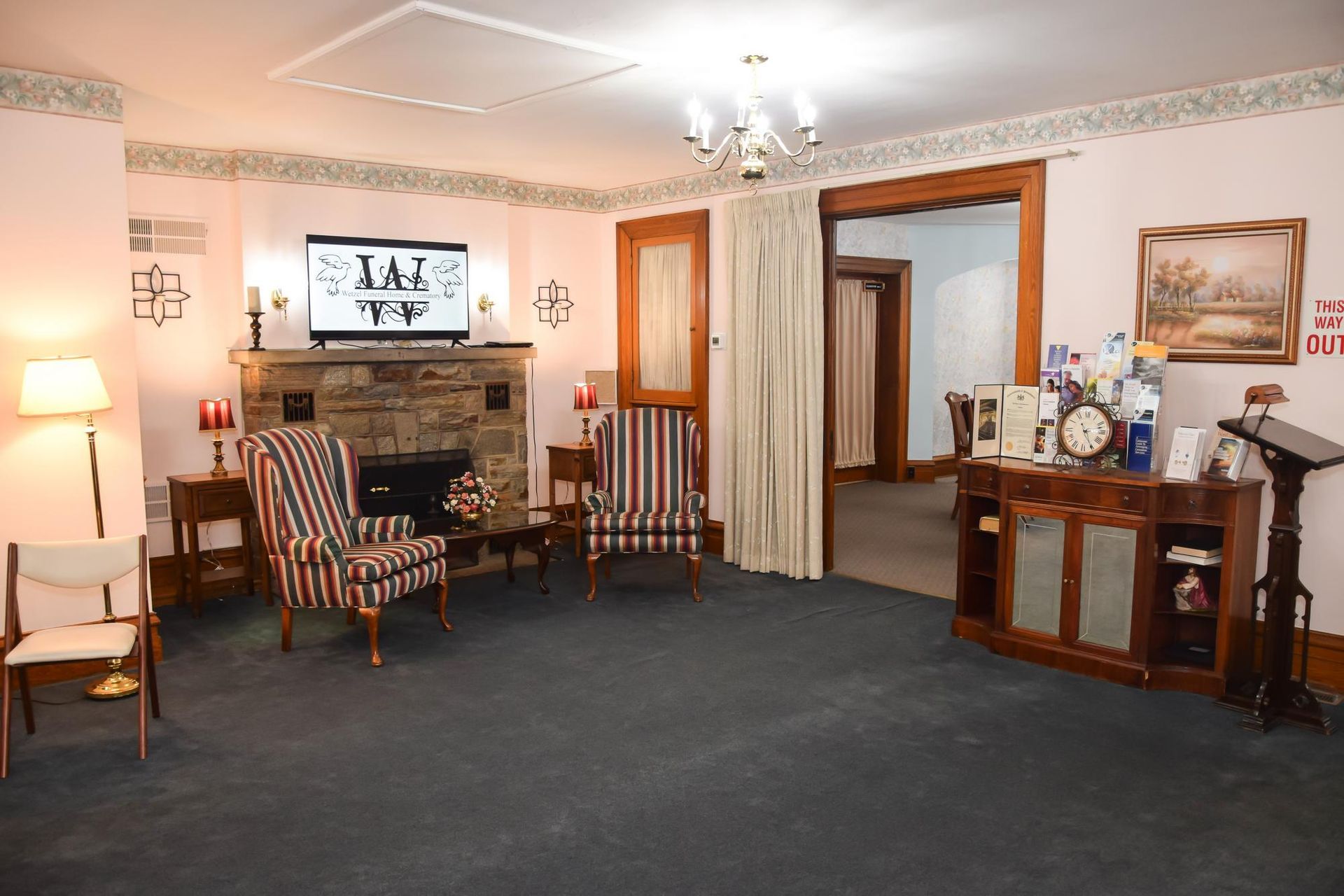 Cozy living room with fireplace, striped armchairs, floor lamp, and wooden cabinet on dark carpet.
