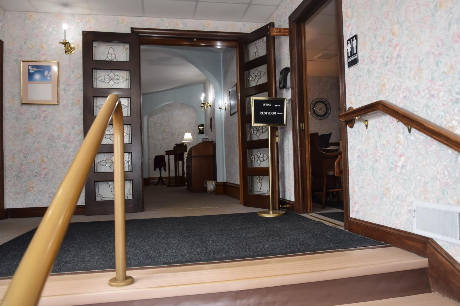 Carpeted hotel lobby entrance with wooden handrails and a doorway into a dining area