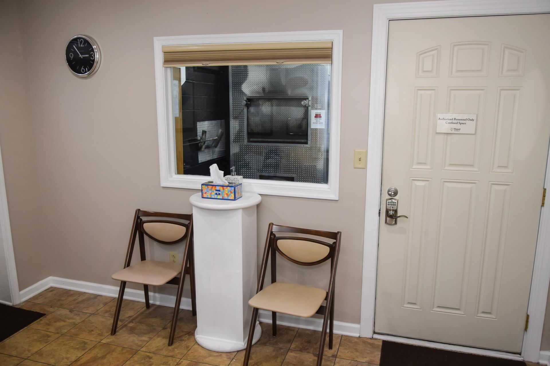 Waiting room with two chairs, a small table, and a service window beside a door.