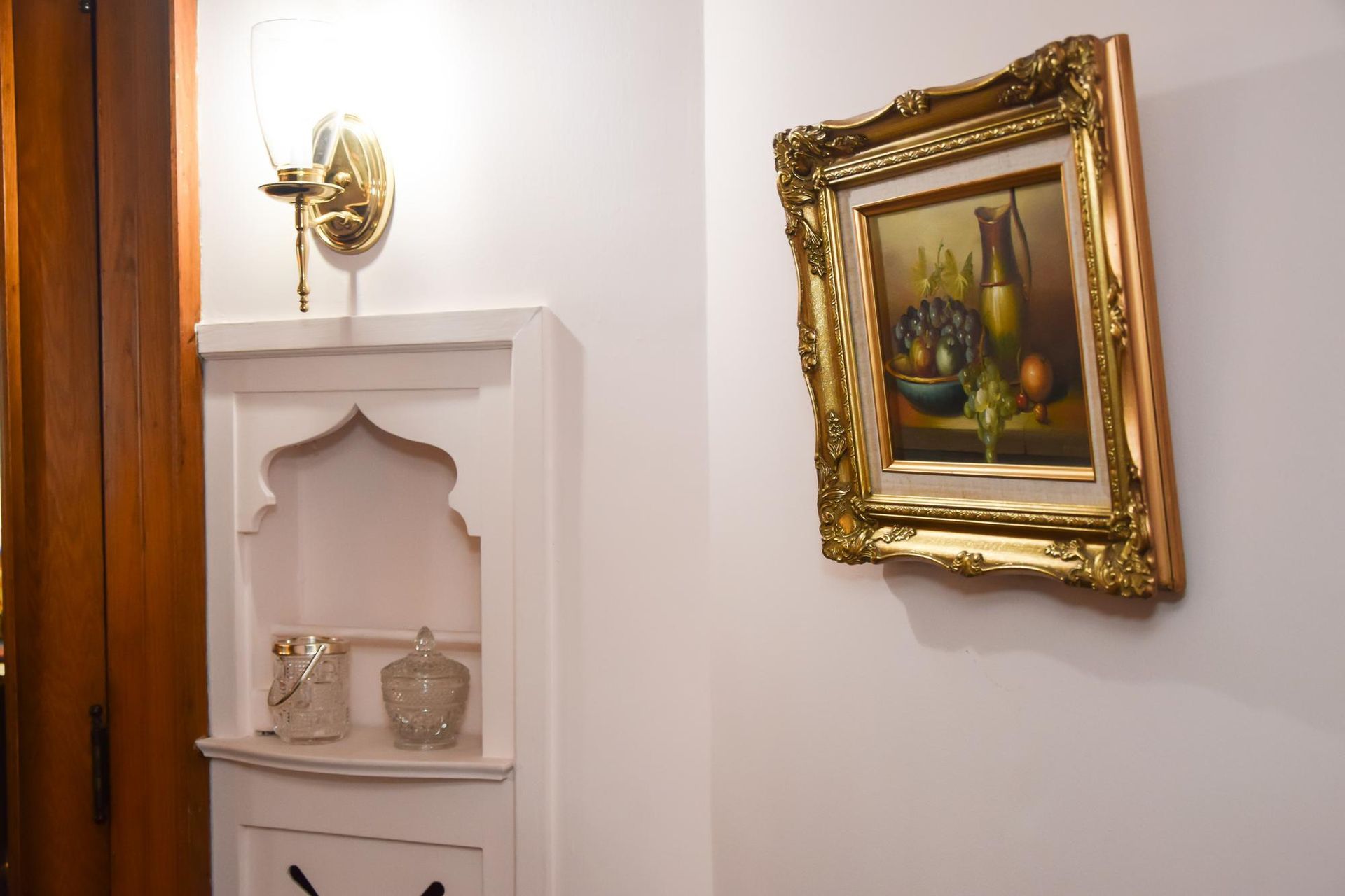 Hallway with a gold wall sconce, white niche shelf, and framed painting on a pale wall