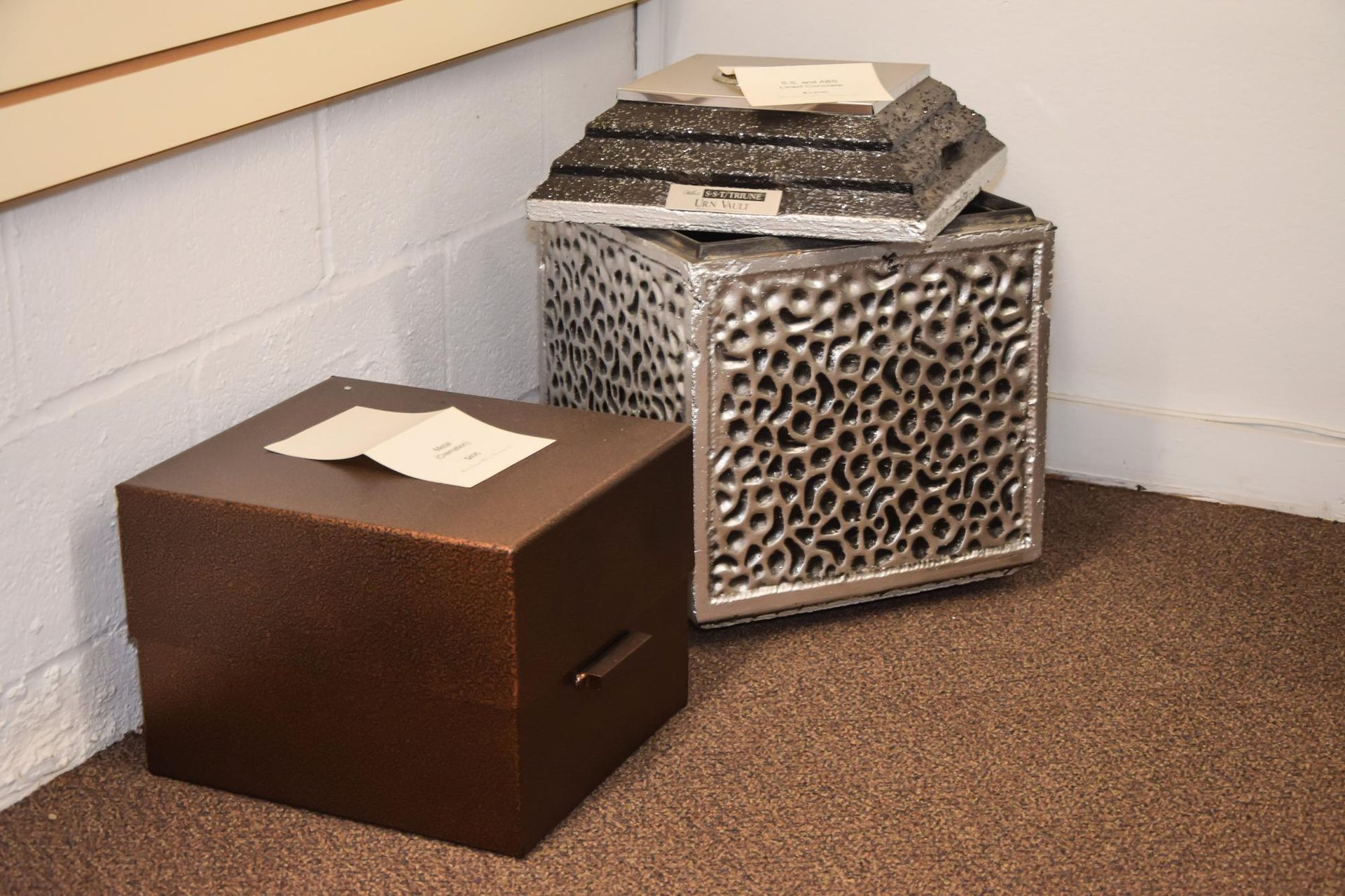 Two decorative storage cubes with papers on top in a carpeted corner by a white wall