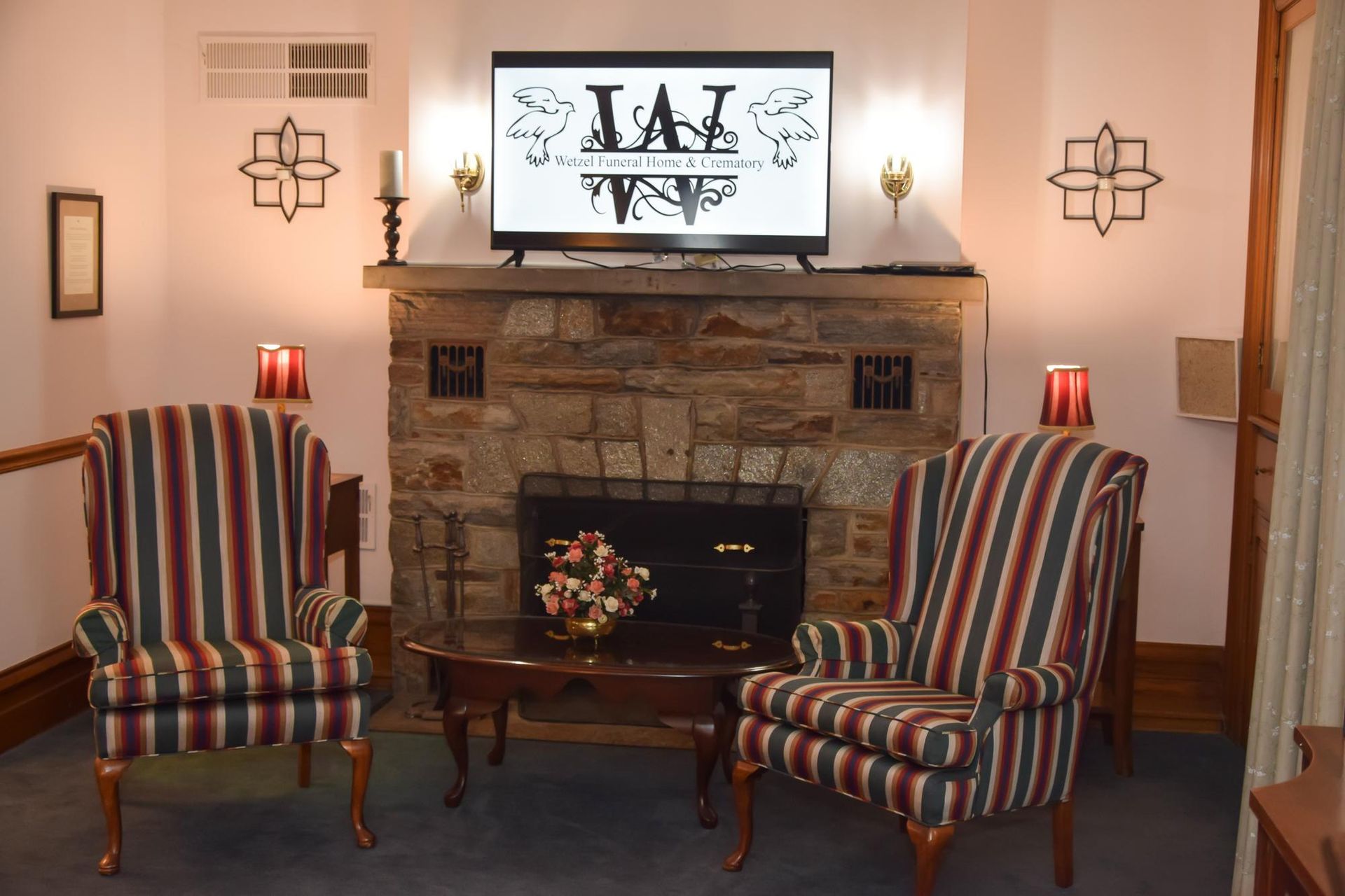 Living room with two striped chairs facing a stone fireplace and a TV above it