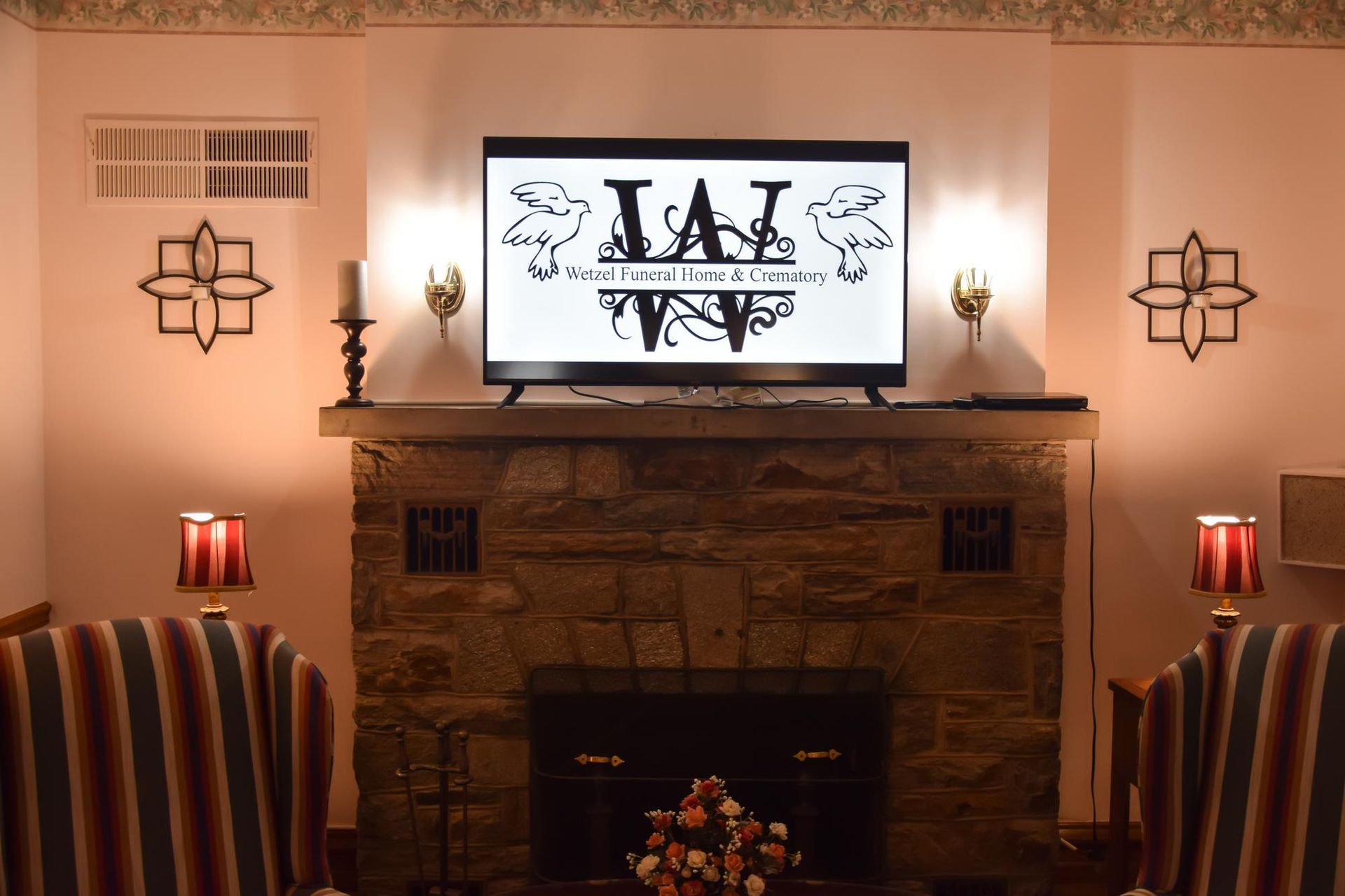 Living room with fireplace, wall art, and a TV displaying a black-and-white logo above the mantel