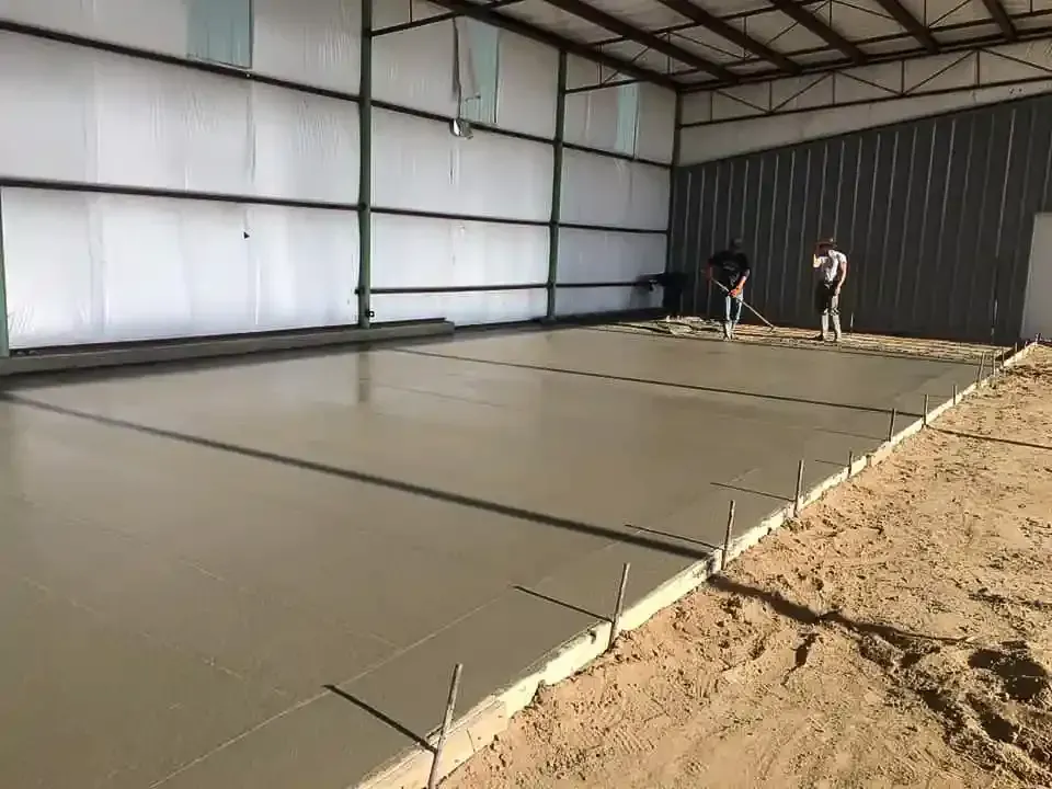 Two men are working on a concrete floor in a building.