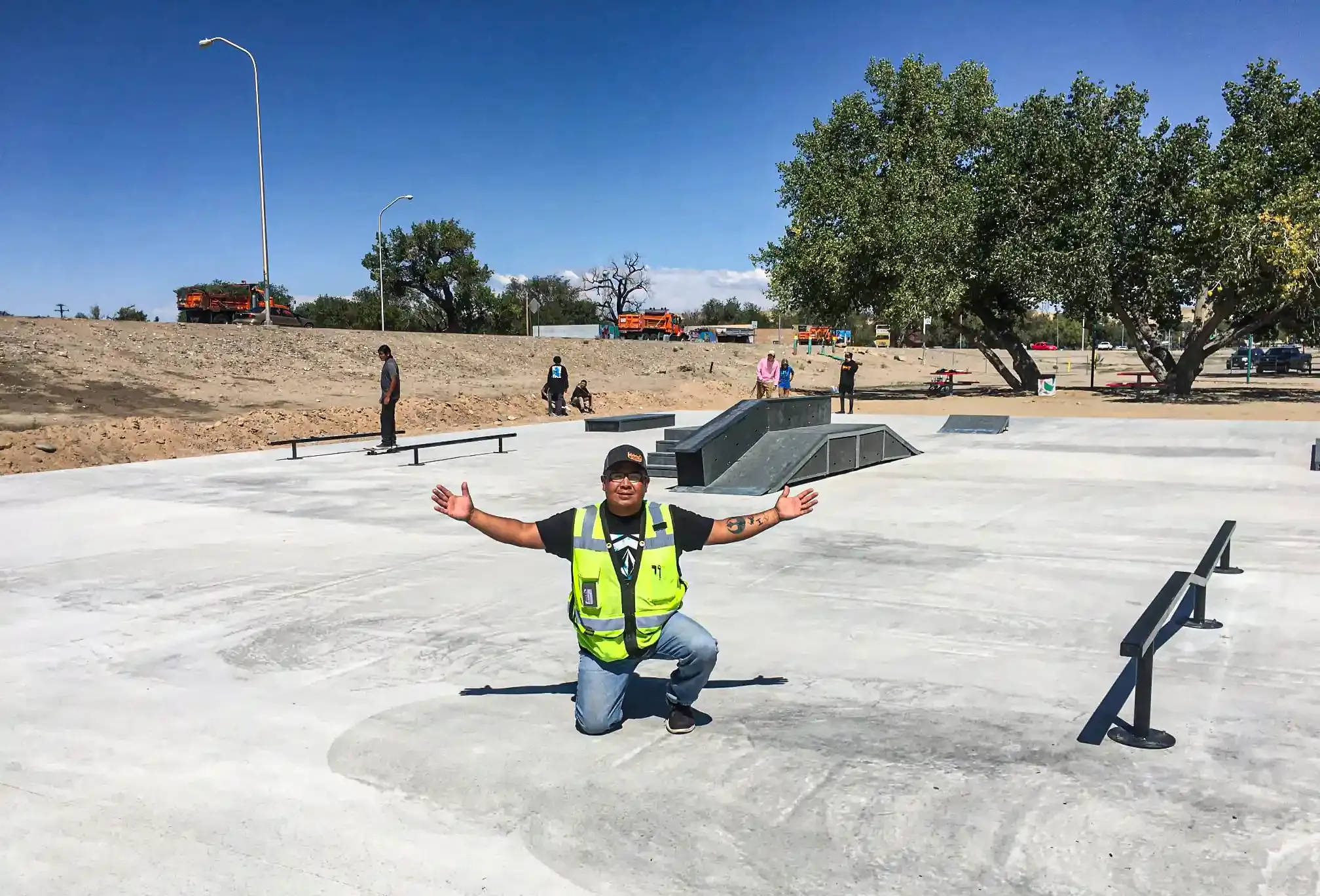 A man in a safety vest is kneeling down in front of a skate park.