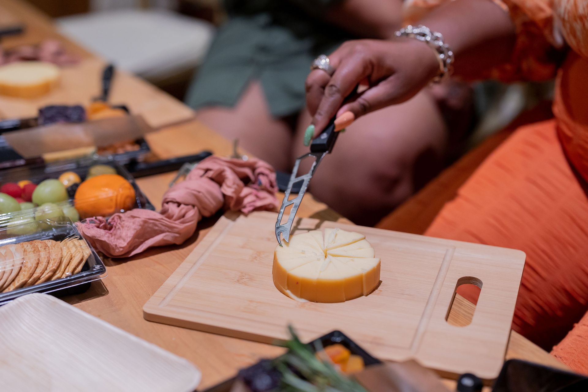 A woman is cutting a piece of cheese on a cutting board.