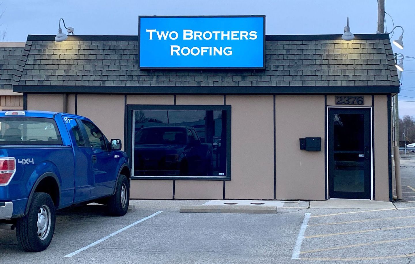 A blue truck is parked in front of a building that says two brothers roofing.
